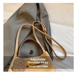 Détail du sac seau en cuir beige avec poignée marron et breloque ours sur un costume gris