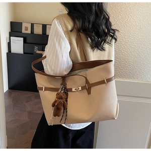 Detail view of large beige canvas tote bag with brown leather straps and plush bear charm