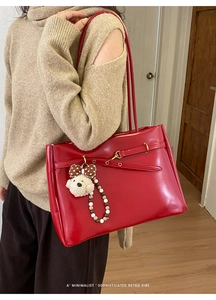 Close-up of red retro tote bag with plush bear charm and beaded detail on a beige knit sweater