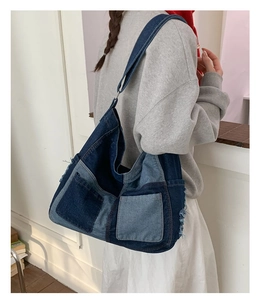 Detail of oversized denim patchwork tote bag showing distressed edges and texture on model