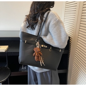 Detail of a large black tote bag with silver hardware and a brown plush bear charm