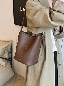 Brown litchi leather bucket bag with adjustable gold buckle strap shown on a model