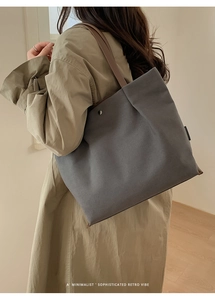 Detail of large canvas tote bag showing brown leather straps and metal snap button closure