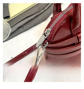 Detail view of deep red glossy leather bag featuring metallic zipper and stitching
