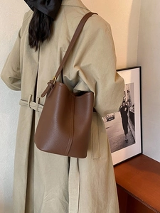 Minimalist brown pebbled leather bucket bag styled with a khaki trench coat for women