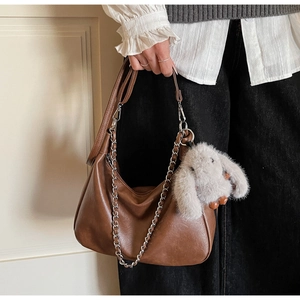 Detail of a brown leather hobo bag with silver chain strap and plush bunny charm accessory