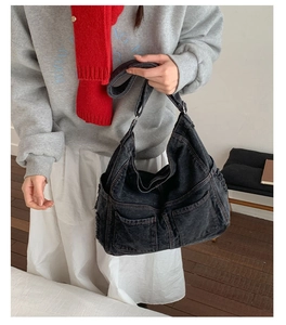 Detail of black denim tote bag with frayed front pockets and adjustable shoulder strap