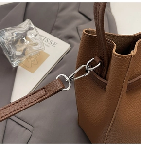 Detailed close-up of silver D-ring and lobster clasp on a brown litchi leather bag