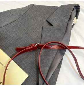 Close-up of a burgundy patent leather skinny belt styled on a grey blazer jacket