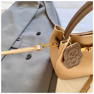 Détail du sac seau en cuir grainé beige avec fermoir doré et pendentif ours décoratif