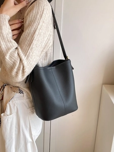 Minimalist black lychee pattern leather bucket bag worn by model with adjustable strap
