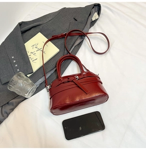 Flat lay of a burgundy semi-circular handbag on a white fabric background with lifestyle props