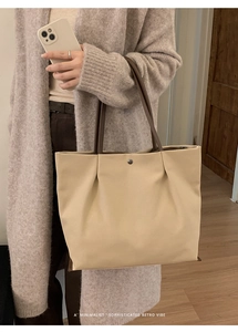 Close-up of minimalist beige tote bag with brown handles and silver metal buckle detail