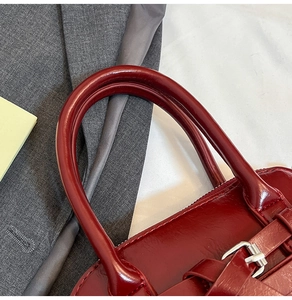 Detail of burgundy glossy leather handbag with silver metal buckle and rounded handle
