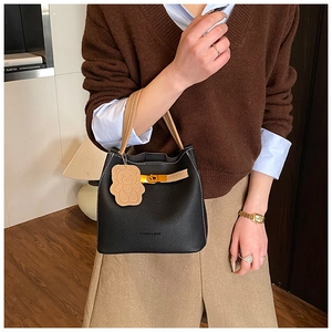 Detalle de bolso cubo de cuero negro granulado con asa marrón y colgante de oso