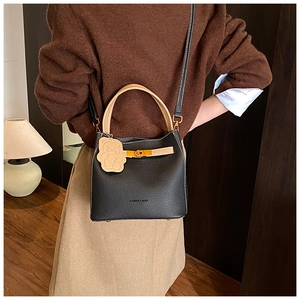 Détail du sac seau en cuir noir avec poignée marron et charmant porte-clés ours