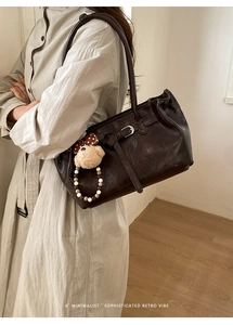 Sophisticated dark brown leather tote bag with a plush bear charm on a beige trench coat