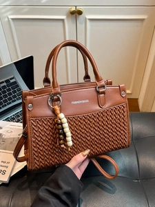 Brown leather tote with woven V-pattern, bead charm, and dual handles shown in a lifestyle set
