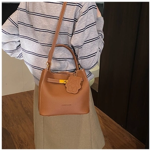 Sac seau en cuir marron avec surpiqûres blanches et pendentif ours porté à l'épaule