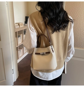 Detail of beige textured leather bucket bag featuring brown straps and silver metal turn-lock