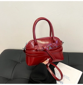 Detail of burgundy shell-shaped handbag showing glossy faux leather and buckle strap decor