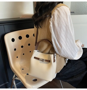 Detail of cream bucket bag with litchi texture, brown leather handle and metal lock