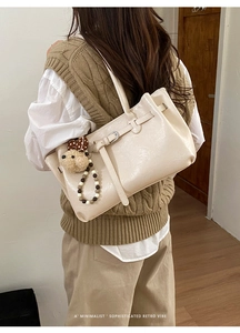Detail of cream shoulder bag featuring glossy finish, buckle strap and cute puppy pendant