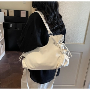 Detail of white leather tote bag with drawstring pleated side pocket and wide shoulder strap