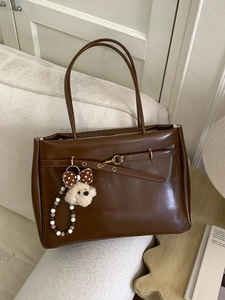 Vintage dark brown leather tote bag with a cute dog pendant on a cozy sofa setting