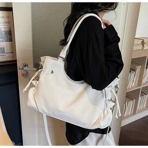 Detail of cream white oversized faux leather tote bag featuring drawstring pleats and wide strap