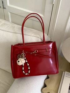 Retro red patent leather tote bag with plush dog charm on a soft cream sofa
