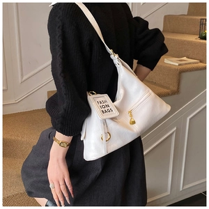 Detail of white leather shoulder bag with gold hardware and fashion tag in daily setting