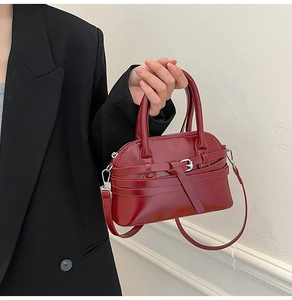 Detail of burgundy glossy leather handbag featuring elegant buckle and shoulder strap