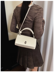 Detail of cream rectangular crossbody bag featuring pebble leather texture and silver twist lock