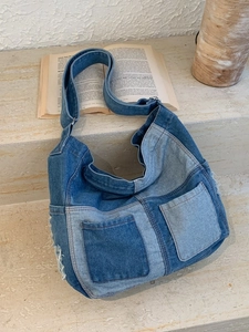 Denim patchwork tote bag with front pockets and frayed tassel details on stone stairs
