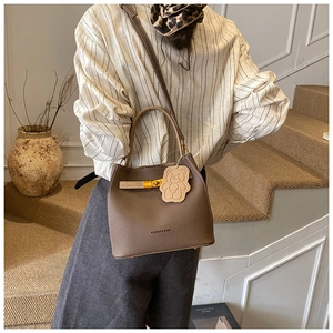 Sac seau marron foncé à motif litchi avec pendentif ours porté sur l'épaule