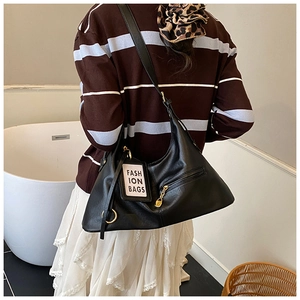 Close-up of black PU leather shoulder bag with gold zipper and fashion tag on model