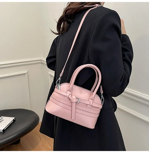 Detail of pink fashion handbag with buckle straps held by model in black suit