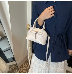 Detail of white patent leather shell bag with belt buckle accent on navy shirt