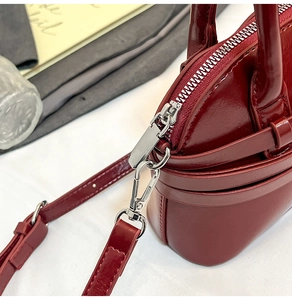Close-up of glossy wine red crossbody bag featuring silver metal zipper and lobster clasp