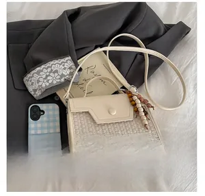 Detail of minimalist cream woven baguette bag with wooden bead charm and shoulder strap