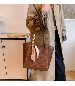 Close-up of brown woven tote bag with smooth leather trim and decorative silk scarf detail