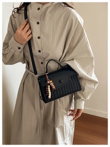Detail of black leather and woven bag featuring a handcrafted wooden bead tassel charm