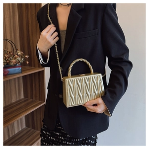 Borsa rigida dorata con texture Matelassé a V e manico a spirale indossata da una modella