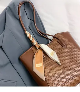 Macro detail of brown woven tote bag featuring decorative fashion silk scarf on the handle