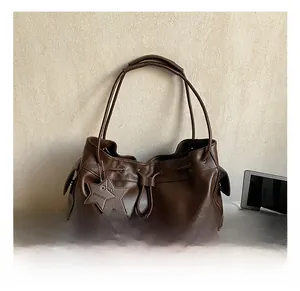 Detail of dark brown pleated tote bag with star charm and drawstring closure on fabric
