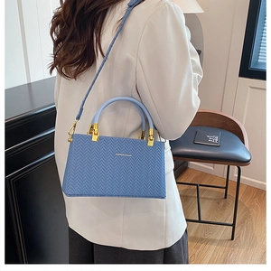 Detail view of woven texture light blue handbag worn by model in elegant cream blazer