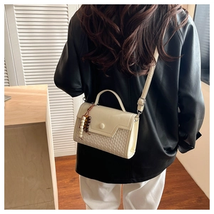 Detail of a cream-colored crossbody bag featuring leather and woven texture with wood beads
