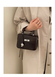 Detail einer dunkelbraunen Lackledertasche mit Silberverschluss und Metallanhänger