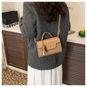 Detailed view of brown woven texture bag with wooden bead charm on a model's back